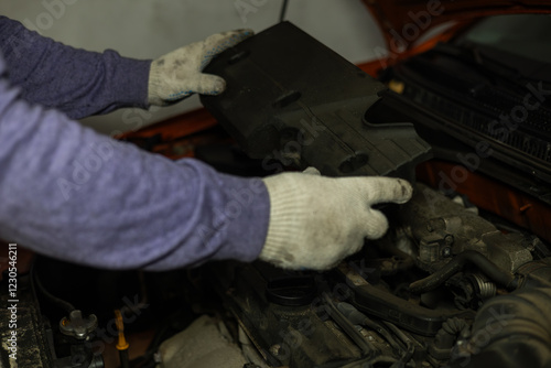 A mechanic wearing protective gloves removes an engine cover in a garage to access and replace spark plugs as part of a routine vehicle maintenance. Replacing spark plugs in cars. photo