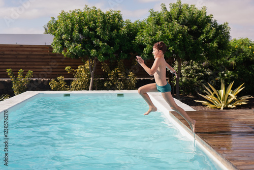 Boy joyfully jumps into refreshing outdoor pool in summer photo