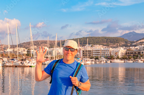 Obraz na płótnie A cheerful man happily poses by the marina, surrounded by numerous sailboats under a stunning beautiful sky. Greece. Rethymnon. Crete. w salonie