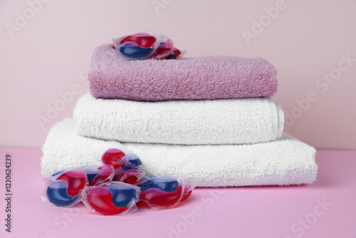 Laundry detergent capsules and clean towel on pink background