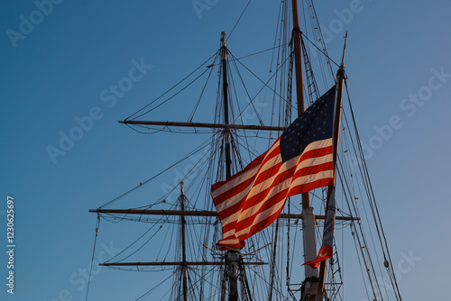 Konstfotografi American Flag flying over Historic Tall Ships along the Harbor under a Cloudless