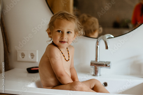 A little boy is sitting in the sink and washing himself.