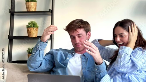 Millennial couple sitting on sofa at home using laptop while celebrating online gambling win with excited gestures and facial expressions during leisure time indoors. People celebrating with laptop