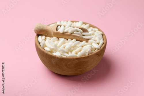 Puffed rice in bowl and scoop on light pink background, closeup photo