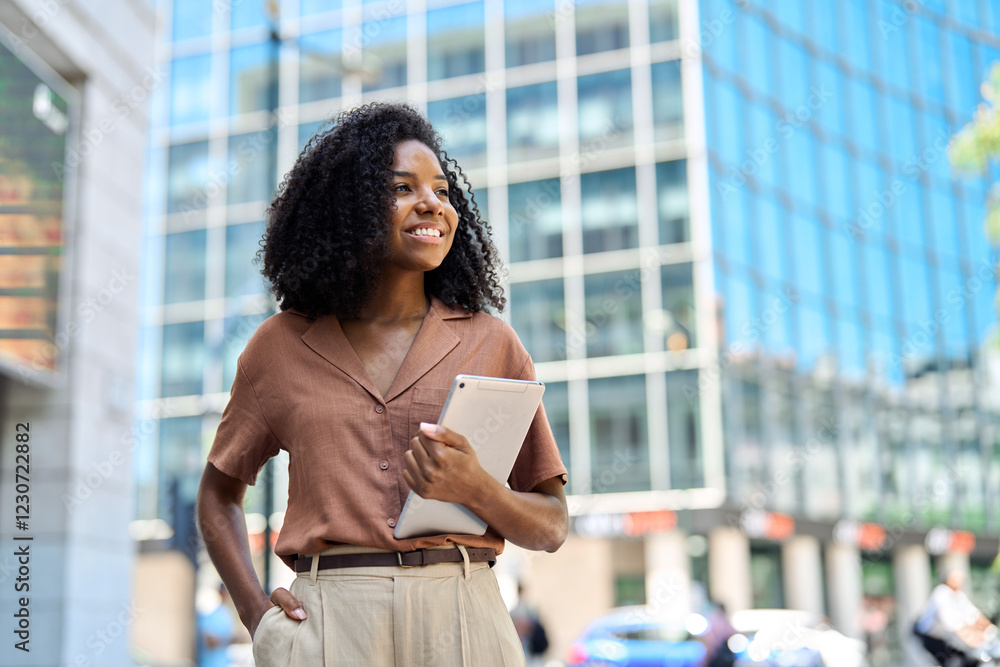 Fototapeta premium Happy confident young African American professional woman, student, female entrepreneur, businesswoman looking away holding tab standing on business city street dreaming of future career. Copy space.