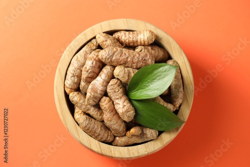 Tumeric rhizomes with leaves in bowl on orange background, top view photo