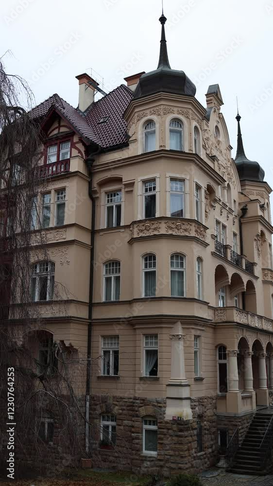Vertical screen: Beautiful historic building with decorative elements, arched balconies, and a steep, ornate roof. Elegant beige facade, stone foundation, and intricate details enhance its architectur Vertical screen: Beautiful historic building with decorative elements, arched balconies, and a steep, ornate roof. Elegant beige facade, stone foundation, and intricate details enhance its architectur