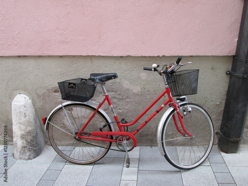 A ladies red push bike with shopping baskets left locked and leaning against a wall in a city A ladies red push bike with shopping baskets left locked and leaning against a wall in a city