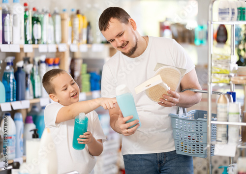 Young man with his son buyers chooses shampoo or shower gel and body washcloth in household chemicals store