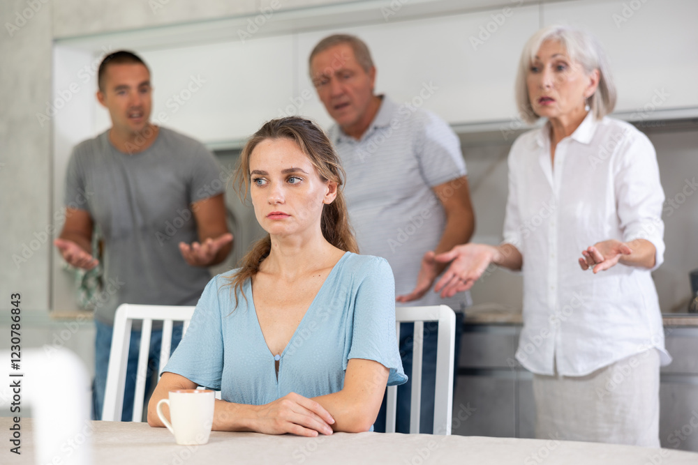 Fototapeta premium Young girl sits at table in kitchen in thought without hearing her family