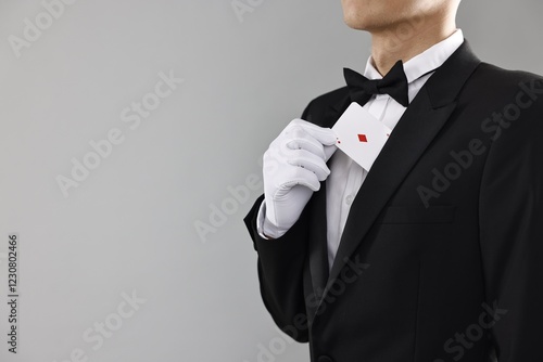 Illusionist hiding playing card behind jacket lapel on grey background, closeup. Space for text photo