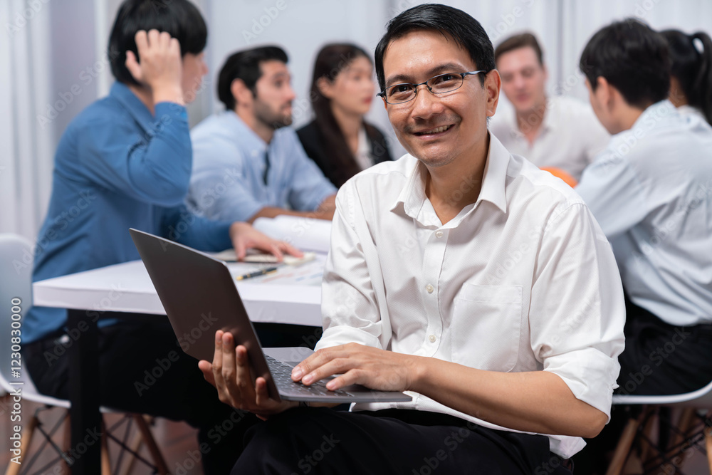 Confidence and happy smiling businessman portrait with background of his colleague and business team working in office. Office worker teamwork and positive workplace concept. Prudent Confidence and happy smiling businessman portrait with background of his colleague and business team working in office. Office worker teamwork and positive workplace concept. Prudent