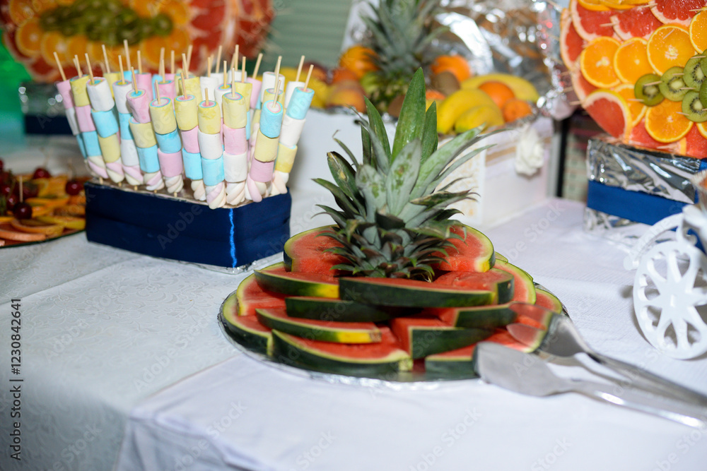 Fototapeta premium A table with a chocolate fountain and various colorful fruits ready to eat with a green led light and a swan shape made of fruit pieces
