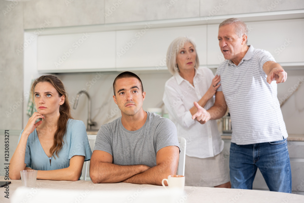 Obraz premium Portrait of an offended married couple in a home kitchen, which mature family members reprimand. Family conflict