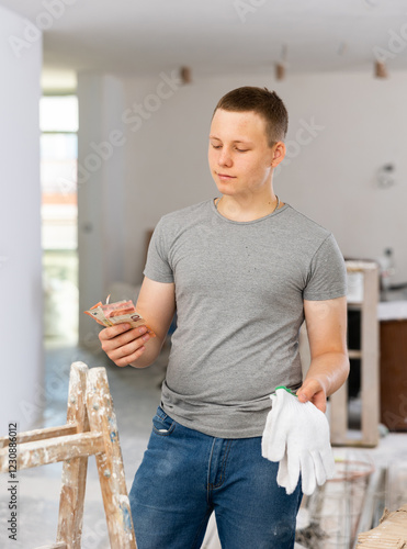 Satisfied fifteen-year-old teenage boy working on a construction site indoors during renovation work in a home, holds the ..first salary in his hands photo