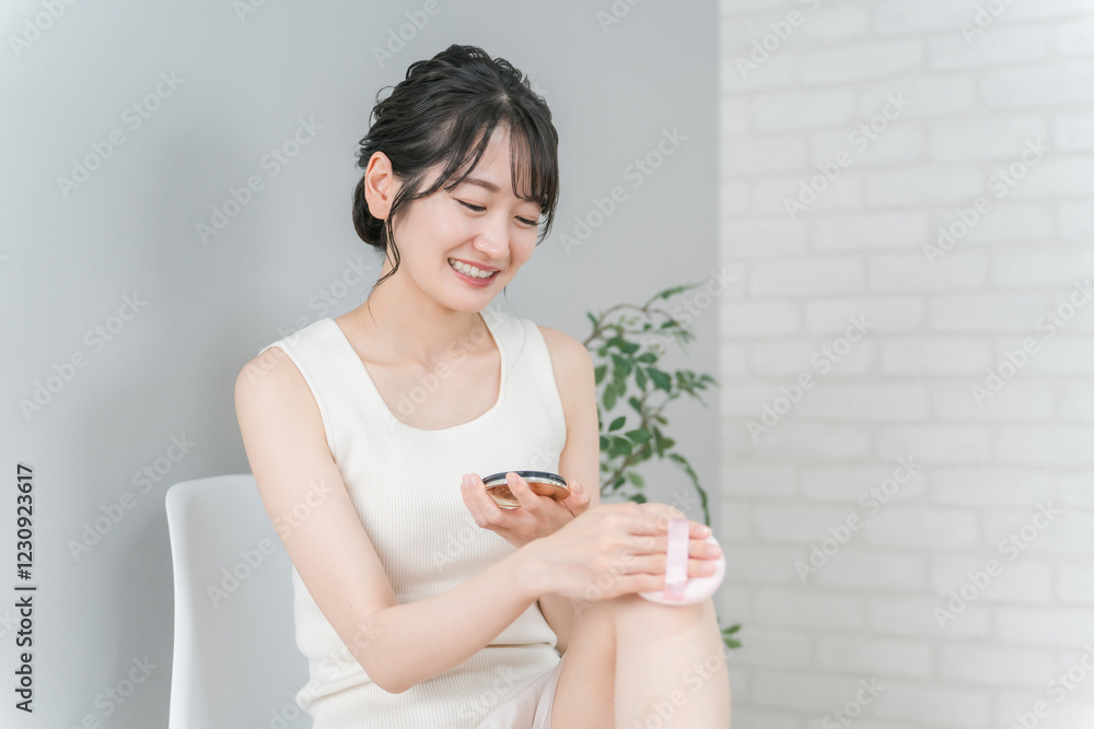 脚に紫外線対策・日焼け止めのボディーパウダーをパフで塗るアジア人女性
