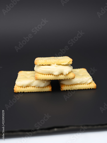 Three square-shaped crackers with a creamy filling stacked on a black surface. photo