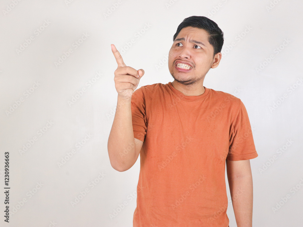 asian man wearing brown t-shirt standing on white background and pointing to the side with worried and shock expression asian man wearing brown t-shirt standing on white background and pointing to the side with worried and shock expression