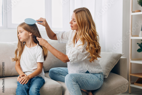 Fotografija Mother and daughter bonding moment woman combing child's hair on a cozy living r