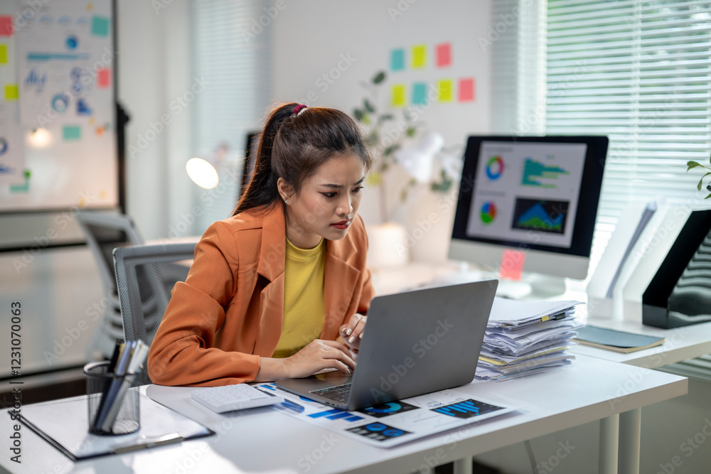 A woman is sitting at a desk with a laptop and a stack of papers A woman is sitting at a desk with a laptop and a stack of papers