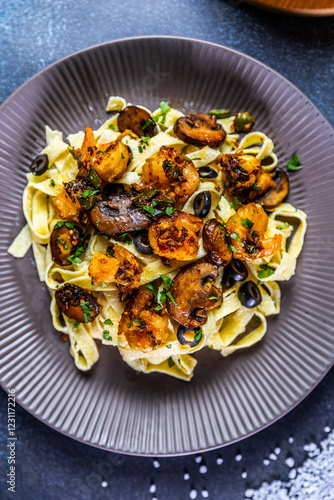 Creamy tagliatelle pasta topped with sautéed shrimp, mushrooms, and black olives, garnished with fresh herbs and Parmesan cheese. photo