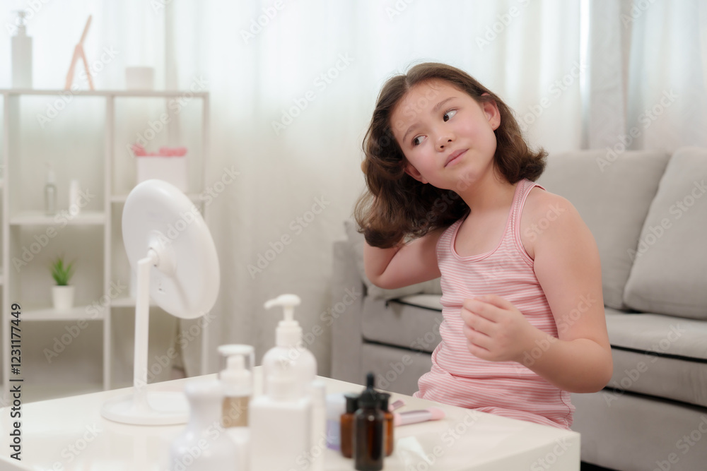 Cute Caucasian girl who loves beauty brushing hair while sitting at a white table with various beauty products. Wearing a pink tank top, adjusting curls in front of a standing mirror. Cute Caucasian girl who loves beauty brushing hair while sitting at a white table with various beauty products. Wearing a pink tank top, adjusting curls in front of a standing mirror.
