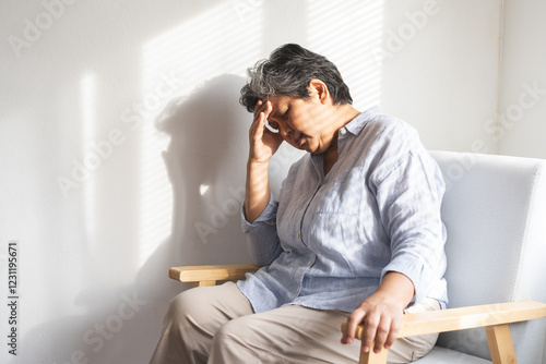 Fotografie Unhappy asian elderly woman sitting on sofa at home, sick and stress headache fe