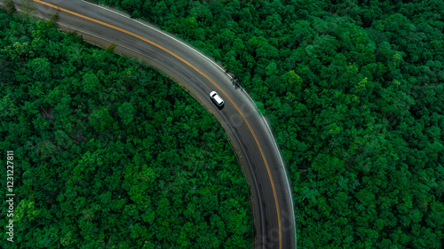Aerial view of dark green forest road and white electric car Natural landscape and elevated roads Adventure travel and transportation and environmental protection concept	
