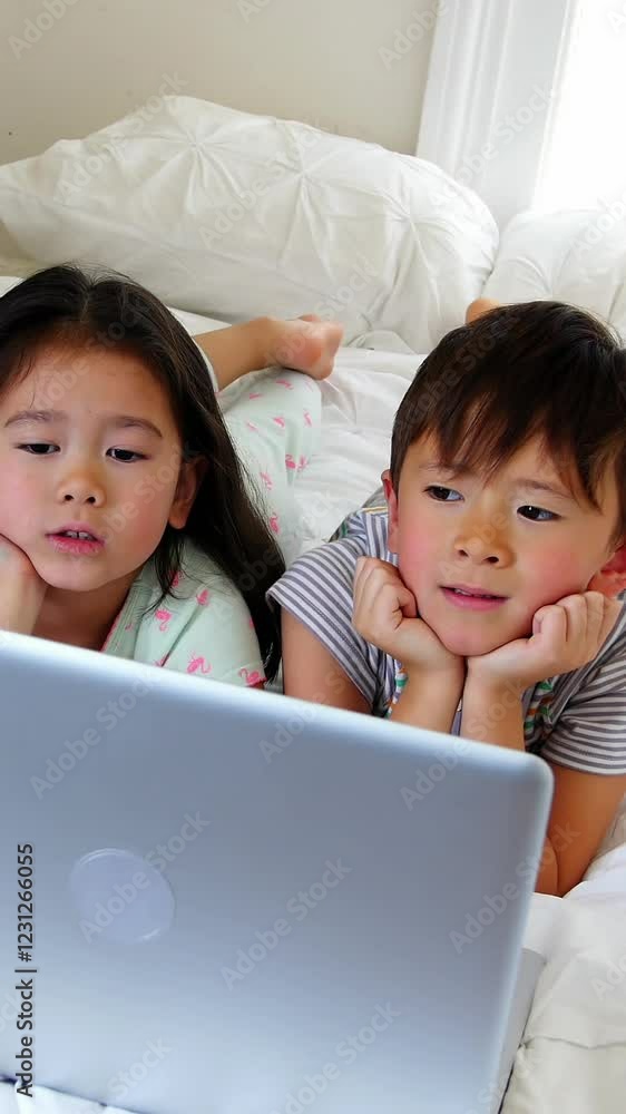 Kids using laptop on bed