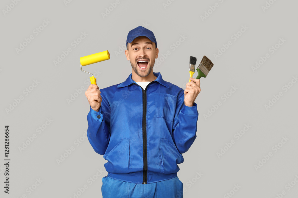 Portrait of cheerful male painter with paint roller and brushes on grey background Portrait of cheerful male painter with paint roller and brushes on grey background