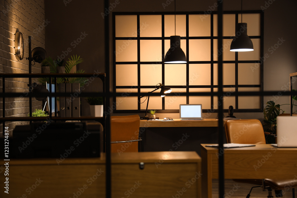 Fototapeta premium Interior of dark office with desks and glowing lamps at night, view through folding screen