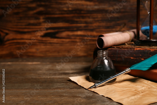 Old books with nib pen, inkwell, scrolls and hourglass on wooden background photo