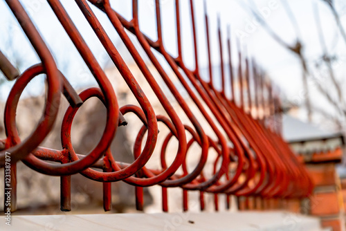 A close-up of a red metal fence with intricate circular and angular patterns. The rusted surface and peeling paint highlight the texture and weathered condition of the structure. 