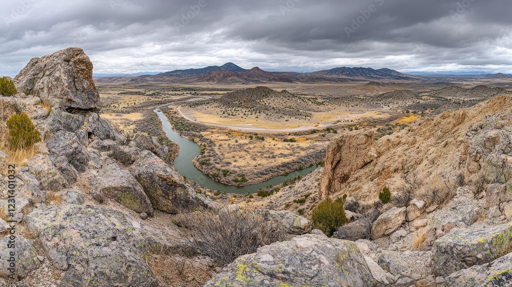 Obraz premium Panoramic view of a river bending through a rocky, desert landscape under a cloudy sky.