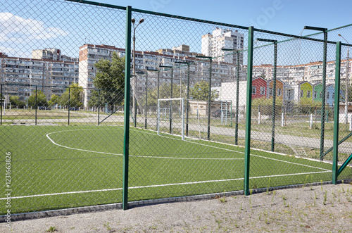 Lawn field for playing football behind the green fence mesh at school territory. Close-up of soccer field with green grass