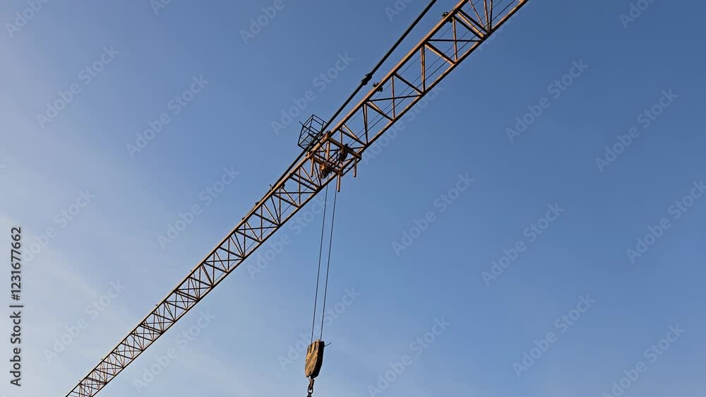 Crane is suspended in the air with a blue sky in the background. The crane is tall and has a lot of metal parts Crane is suspended in the air with a blue sky in the background. The crane is tall and has a lot of metal parts