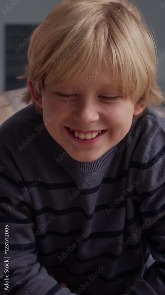 Vertical shot of cheerful Caucasian boy making paper crafts with parent at table in living room