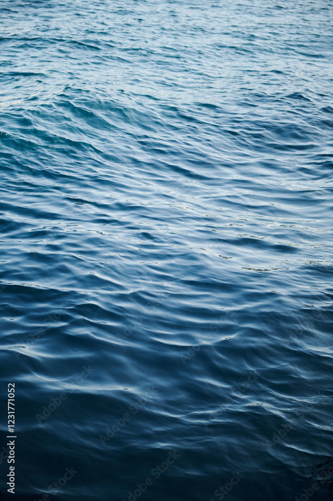 Calm blue ocean water surface with gentle waves and ripples under natural sunlight, creating a peaceful and serene marine atmosphere Calm blue ocean water surface with gentle waves and ripples under natural sunlight, creating a peaceful and serene marine atmosphere