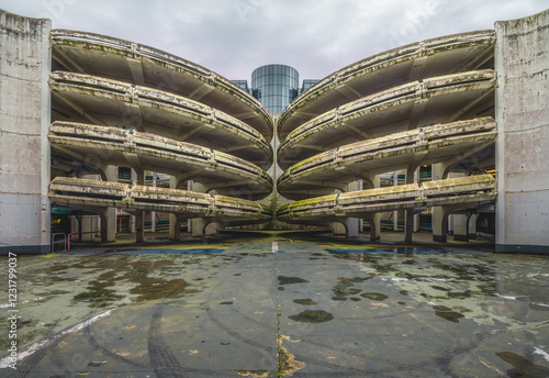 Parking abandonné à l’architecture brutaliste, marqué par le temps et la végétation envahissante. Symétrie saisissante, textures usées et atmosphère post-apocalyptique capturant l’esthétique de l’aban