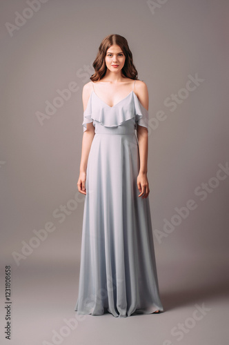 Attractive cheerful young lady in blue bardot evening dress. Studio portrait of romantic brunette woman. Bardot maxi gown with deep neckline, elegant look. Sensual bridesmaid's summer outfit