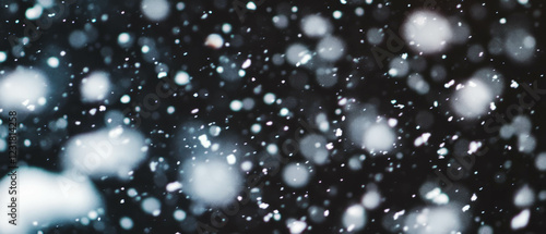 Soft snowfall with thawing patches signaling spring against a dark background