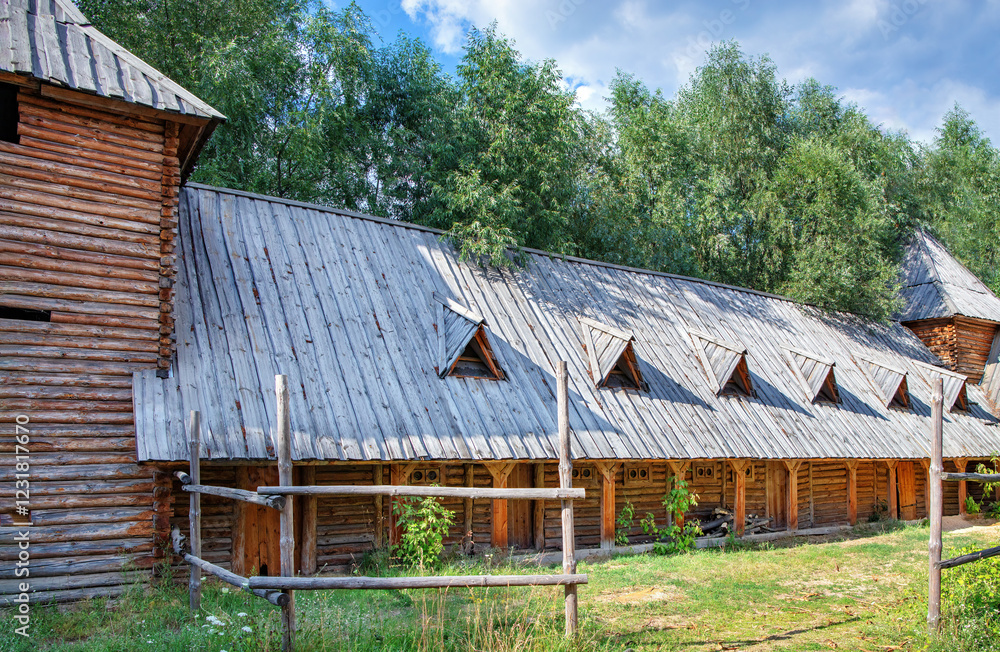 Wooden structures bask in sunlight near lush green trees in a serene landscape