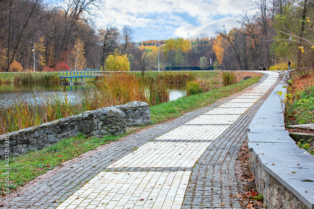 Walking along the tranquil lakeside path surrounded by autumn colors and gentle clouds