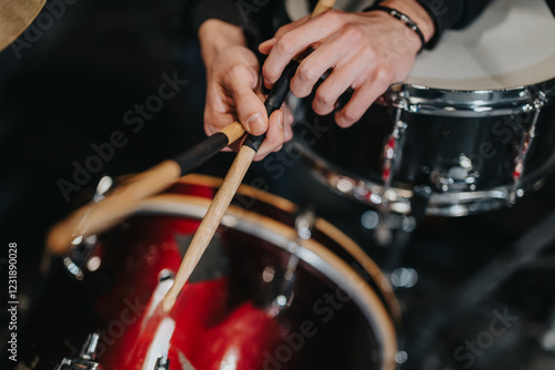 Hands of a musician playing drums with drumsticks on a vibrant red drum set, showcasing skillful technique in a musical studio setting. photo