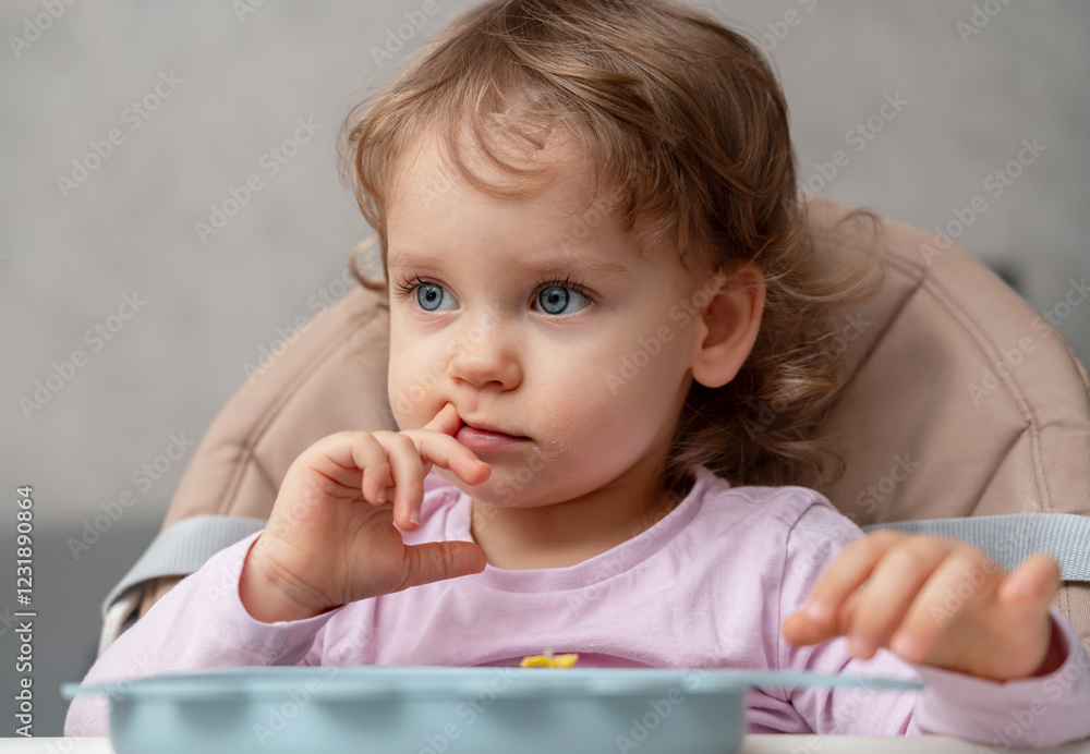 A thoughtful toddler sitting at the table, observing her surroundings in a cozy home setting A thoughtful toddler sitting at the table, observing her surroundings in a cozy home setting