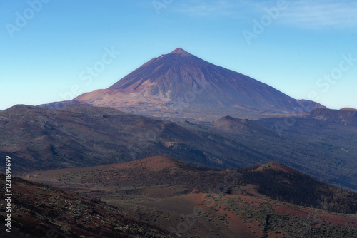 Vue panoramique du volcan Teide à Tenerife, plus haut sommet d’Espagne. Paysage volcanique spectaculaire, contrastes de couleurs entre roches noires et rouges sous un ciel bleu limpide.