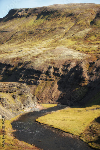Paysage sauvage d'Islande avec une rivière sinueuse serpentant à travers des collines aux couleurs automnales. Relief accidenté, contrastes de lumière et nature préservée caractérisent cette scène uni