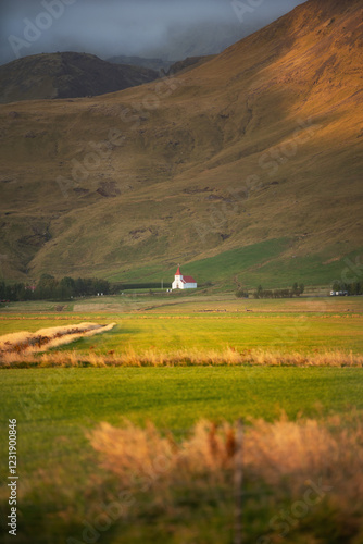 Petite église isolée au pied d’une montagne en Islande, baignée par la lumière dorée du soir. Un paysage sauvage et paisible où l’architecture traditionnelle se fond dans un décor naturel époustouflan