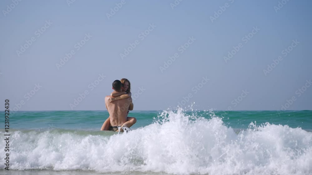Fit man carrying woman in sea surf waves, water makes splashes. Happy couple in love having fun in the ocean. Tanned boyfriend and girlfriend enjoying romantic trip in the peaceful place. Fit man carrying woman in sea surf waves, water makes splashes. Happy couple in love having fun in the ocean. Tanned boyfriend and girlfriend enjoying romantic trip in the peaceful place.