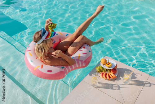 Woman relaxing in swimming pool eating grapes and enjoying summer fruit plate photo